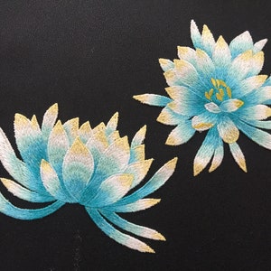 Könnte beinhalten: Zwei gestickte blaue und weiße Blumen mit gelben Akzenten auf schwarzem Hintergrund.