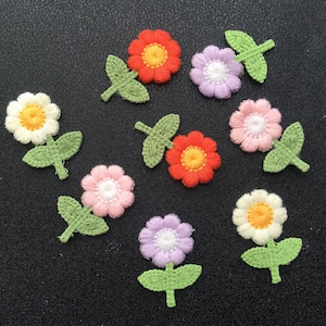 May include: Nine embroidered felt flower appliques with green leaves. The flowers are in various colours, including pink, white, yellow, orange, and purple.