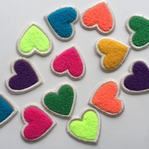 Può includere: Una collezione di 12 toppe a forma di cuore in feltro di vari colori, tra cui verde, blu, rosa, arancione, giallo e viola. Ogni cuore ha un contorno bianco e misura circa 5 cm di diametro.