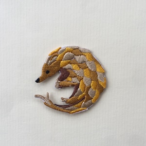 May include: A brown and yellow embroidered patch of a curled up pangolin.