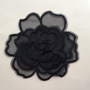 Peut inclure: Applique de fleur en tissu noir transparent avec un design en couches. La fleur a un centre avec un petit groupe de perles.