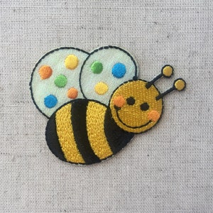 May include: Embroidered bee patch with yellow and black stripes, a smiling face, and white wings with colourful polka dots.