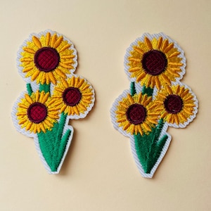 Könnte beinhalten: Zwei gestickte Bügelbilder mit einem Cluster aus drei gelben Sonnenblumen mit burgunderfarbenen Zentren und grünen Stielen.