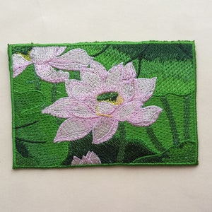 Könnte beinhalten: Gestickter Aufnäher mit rosa Lotusblumen mit gelben Zentren auf grünem Blattwerk.