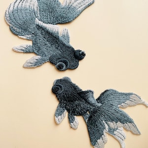 May include: Two embroidered iron-on patches of black and white goldfish. The fish are in a swimming position with their tails fanned out.