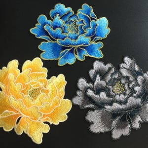Pode incluir: Três patches de flores bordadas em tecido azul, amarelo e cinza. As flores são todas peônias com pontos de costura detalhados.