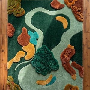 May include: A rectangular rug with a nature-inspired design. The rug features a dark green background with a lighter green river-like shape winding through it. Various textured shapes in shades of brown, orange, yellow, and teal are scattered across the surface.