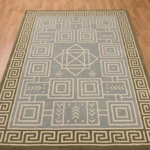 May include: A rectangular area rug featuring a light blue background with a white geometric pattern of nested squares, arrows, and a central diamond motif. The rug is framed by a wide border with a repeating white Greek key pattern on a tan base.