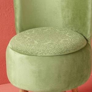 Könnte beinhalten: Hellgrüner Samtstuhl mit rundem Sitz und Rückenlehne. Das Sitzkissen hat ein gemustertes Design. Der Stuhl hat drei Holzbeine. Der Stuhl ist ein stilvolles Möbelstück.