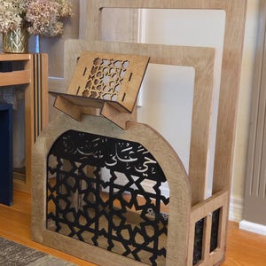 May include: A wooden book stand with a decorative arch and intricate cutouts. The stand is made of light brown wood and has a black metal insert. The stand is designed to hold books or other items.