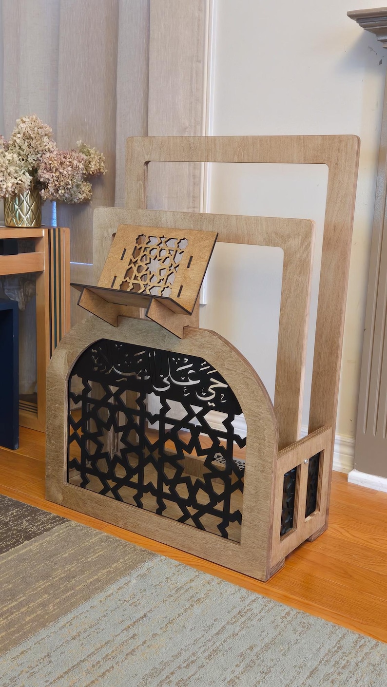 May include: A wooden book stand with a decorative arch and intricate cutouts. The stand is made of light brown wood and has a black metal insert. The stand is designed to hold books or other items.