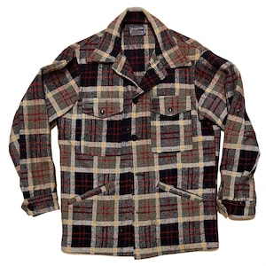 Può includere: Una camicia di flanella a quadri rossi, neri e beige con chiusura a bottoni e due grandi tasche. La camicia ha un'etichetta che recita "Pendleton."