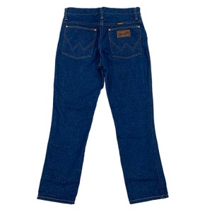K&ouml;nnte beinhalten: Dunkelblaue Jeans aus Denim mit klassischem F&uuml;nf-Taschen-Design. Mit dem Wrangler-Logo auf einem braunen Lederaufn&auml;her und charakteristischen N&auml;hten auf den Ges&auml;&szlig;taschen. Die Jeans hat einen geraden Beinverlauf und einen Knopf- und Rei&szlig;verschluss.