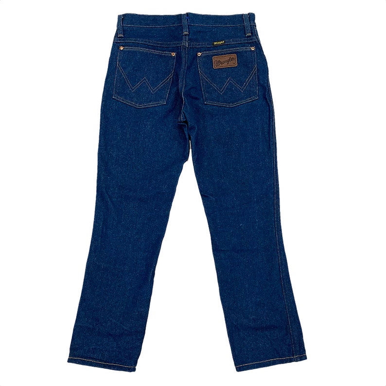 K&ouml;nnte beinhalten: Dunkelblaue Jeans aus Denim mit klassischem F&uuml;nf-Taschen-Design. Mit dem Wrangler-Logo auf einem braunen Lederaufn&auml;her und charakteristischen N&auml;hten auf den Ges&auml;&szlig;taschen. Die Jeans hat einen geraden Beinverlauf und einen Knopf- und Rei&szlig;verschluss.
