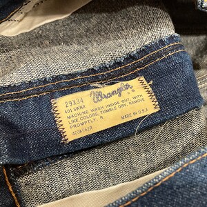 K&ouml;nnte beinhalten: Nahaufnahme einer blauen Jeans. Das Etikett zeigt die Marke "Wrangler", die Gr&ouml;&szlig;e 29x34 Zoll und Waschanweisungen. Die Jeans ist in den USA hergestellt.