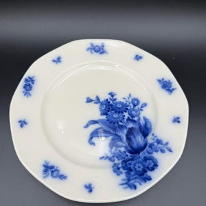 May include: White porcelain plate with a scalloped edge, adorned with a blue floral design. The plate features a central bouquet and smaller floral accents around the rim. A classic piece for serving or display.