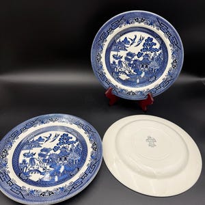 May include: Three blue and white Willow pattern plates. Two plates are face up, displaying the intricate design of a landscape with buildings, trees, and birds. The third plate is face down, revealing a plain white surface.