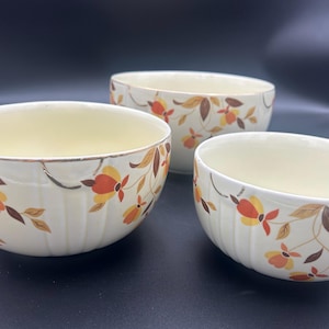 May include: Three vintage ceramic bowls with a cream-colored interior and a white exterior. The bowls are decorated with a floral pattern in shades of orange, yellow, and brown. The bowls have a ribbed design and a gold rim.