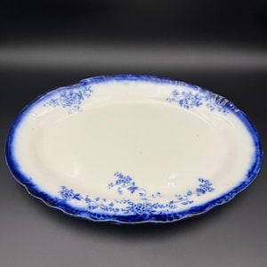 May include: An oval, antique serving platter with a white center and a deep blue, scalloped edge. Delicate blue floral patterns adorn the rim. The platter is likely made of ceramic or porcelain.