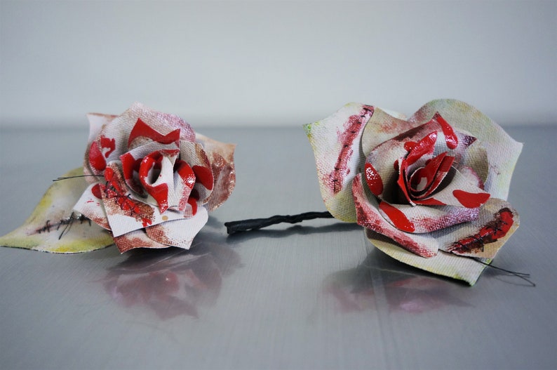 May include: Two white fabric roses with red painted accents and stitched details. The roses are distressed and have a vintage look.