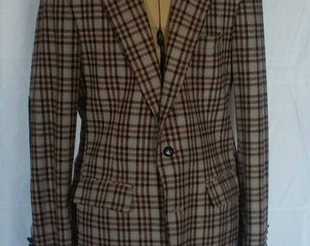 May include: A tan and brown plaid blazer with a single-button closure, two front pockets, and a notched lapel. The jacket is displayed on a mannequin. The sleeves have three buttons. The plaid pattern is a classic design.