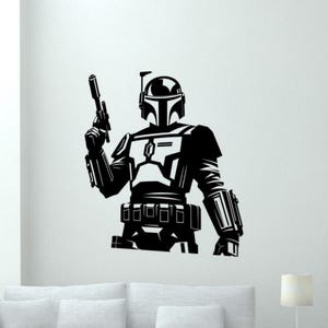Könnte beinhalten: Schwarz-weiße Grafik eines Mandalorianischen Kriegers mit einem Blaster. Die Figur steht in einer aufrechten Position und trägt eine detaillierte Rüstung und einen Helm. Ideal für Wandkunst oder Aufkleber.