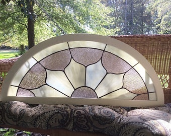 May include: A semi-circular stained glass window panel featuring a sunburst pattern with alternating clear textured glass and opaque white glass segments, all encased within a smooth, light-colored arched wooden frame.