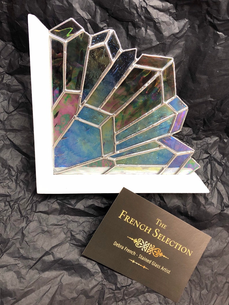 May include: A stained glass art piece with iridescent, geometric shapes in shades of blue, green, and purple, set within a white frame. The piece is a corner design. A business card reads "The French Selection - Debra French - Stained Glass Artist."