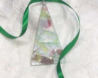 May include: A green ribbon hangs from a glass Christmas tree ornament. The ornament is shaped like a triangle and is made of mosaic glass in shades of green, pink, and white.