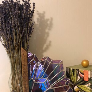 May include: A stained glass art piece with a geometric design in shades of purple, blue, and green, set in a wooden frame. A vase of dried lavender and a decorative box with a gold sphere are also in the image.