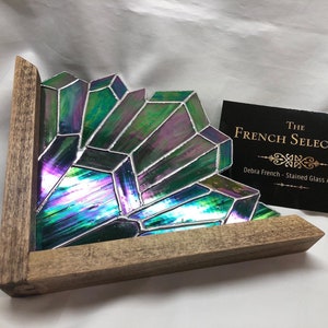 May include: Iridescent stained glass art piece in a geometric crystal design, set in a wooden frame. The glass features shades of green, purple, and blue. The piece is displayed with a business card that reads "The French Selection".