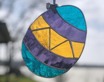 May include: A stained glass Easter egg ornament with a teal, purple, and yellow geometric design.