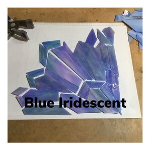 May include: Blue iridescent glass pieces arranged in a geometric pattern. The pieces are various shades of blue and purple, with a shimmering, iridescent quality. The text "Blue Iridescent" is displayed below the glass.
