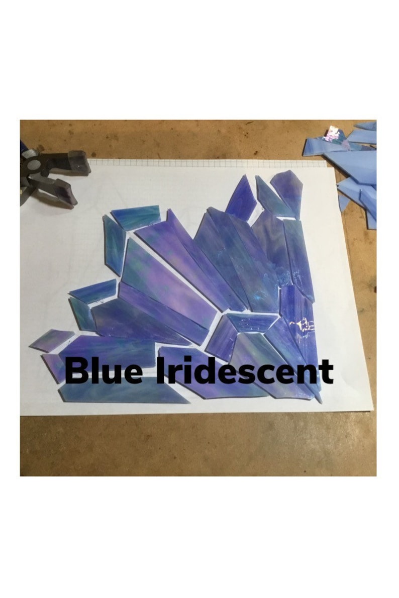 May include: Blue iridescent glass pieces arranged in a geometric pattern. The pieces are various shades of blue and purple, with a shimmering, iridescent quality. The text "Blue Iridescent" is displayed below the glass.