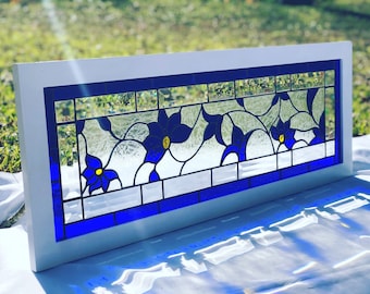 May include: A rectangular stained glass window with a white frame. The design features blue flowers with yellow centers and clear glass, outlined with black lines. The window is approximately 30 inches long.