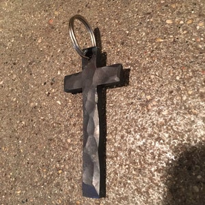 May include: A black metal cross keychain with a hammered finish. The cross is attached to a silver key ring.