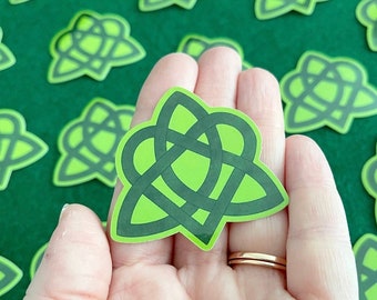 May include: A green Celtic knot sticker with a heart shape in the centre. The sticker is on a green felt background.