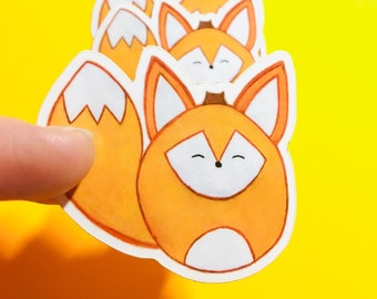 Op de afbeelding: Een rij oranje en witte vossen stickers met glimlachende gezichten. De stickers zijn op een gele achtergrond.