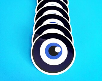 May include: A row of blue and white evil eye stickers with a black pupil. The stickers are arranged vertically on a blue background.