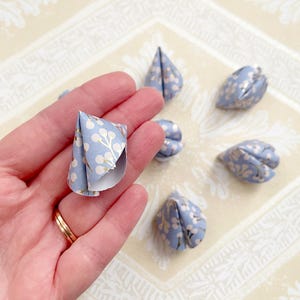 May include: A set of seven blue and white origami fortune cookies with a floral pattern. The fortune cookies are folded into a traditional cone shape.