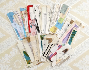 Könnte beinhalten: Eine Sammlung verschiedener Papierephemera, darunter zerrissene Papierstreifen mit dekorativen Nähten. Einige Streifen weisen florale Muster, Noten und Text in verschiedenen Sprachen auf. Die Farbpalette umfasst Weiß, Beige, Blau, Rosa und Grün.