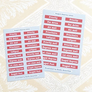 Può includere: Due fogli di etichette postali con sfondo azzurro chiaro e testo rosso. Le etichette includono termini come "Prioritario", "Par Avion" e "Express Mail". Il testo "Seagull Express labels" è in alto. Illustrazione di Studio Amarillys.