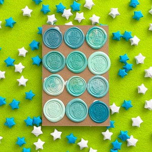May include: A sheet of blue and white wax seals featuring a hamsa hand design. The seals are arranged in a grid pattern on a green background.