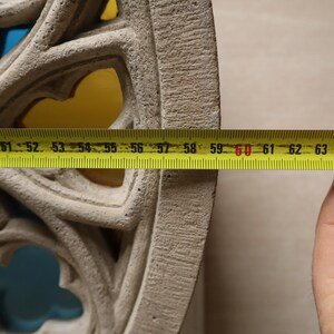 May include: Close-up of a section of a light gray, intricately carved stone architectural element. A yellow measuring tape shows a measurement of approximately 10 inches. The element has a repeating pattern of arched openings.