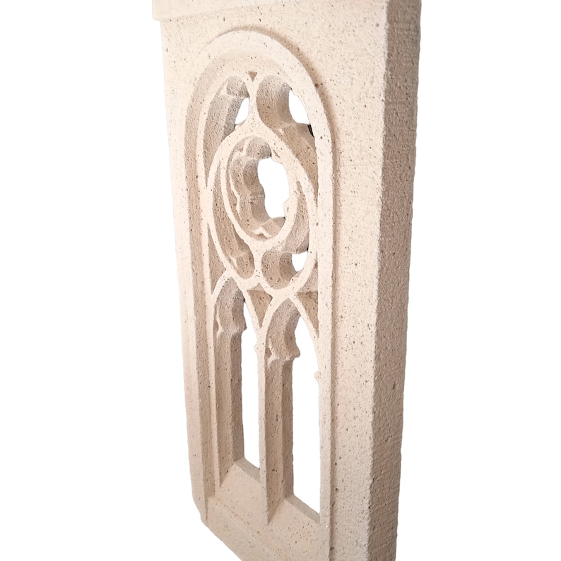 May include: A white stone window frame with a decorative, intricate design. The frame is made of a rough, textured material and has a slightly arched top.