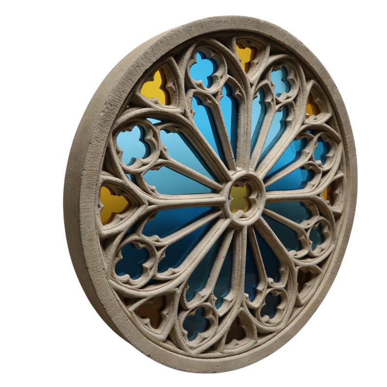 May include: A round, beige stone architectural element with a stained glass design. The stained glass features blue and yellow sections, creating a vibrant contrast. The design is symmetrical, with a central circular element and radiating patterns.