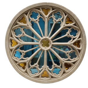 May include: A round, beige-colored architectural element with a stained glass design. The glass features blue and yellow sections arranged in a radial pattern. The frame has a detailed, gothic-style tracery.