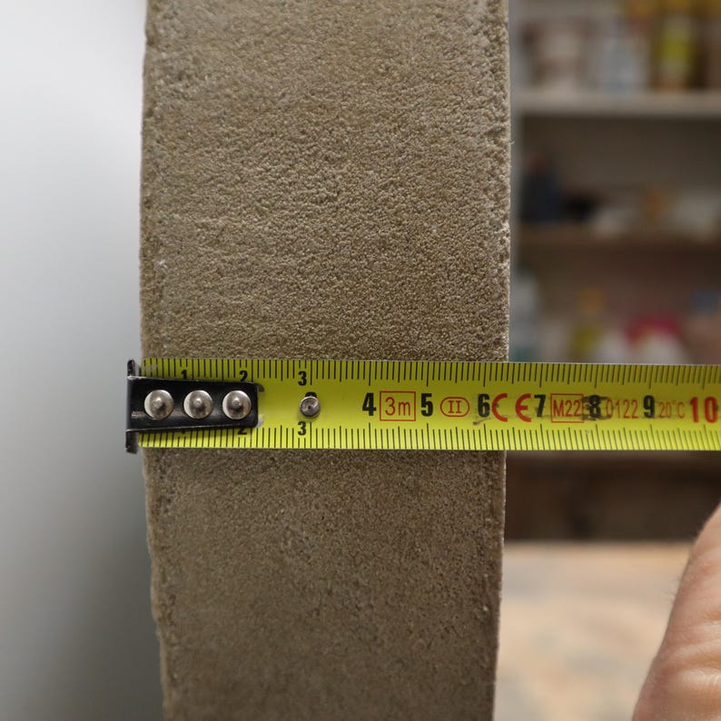 May include: A close-up of a beige, textured rectangular object being measured with a yellow tape measure. The tape measure shows a measurement of approximately 3 inches.