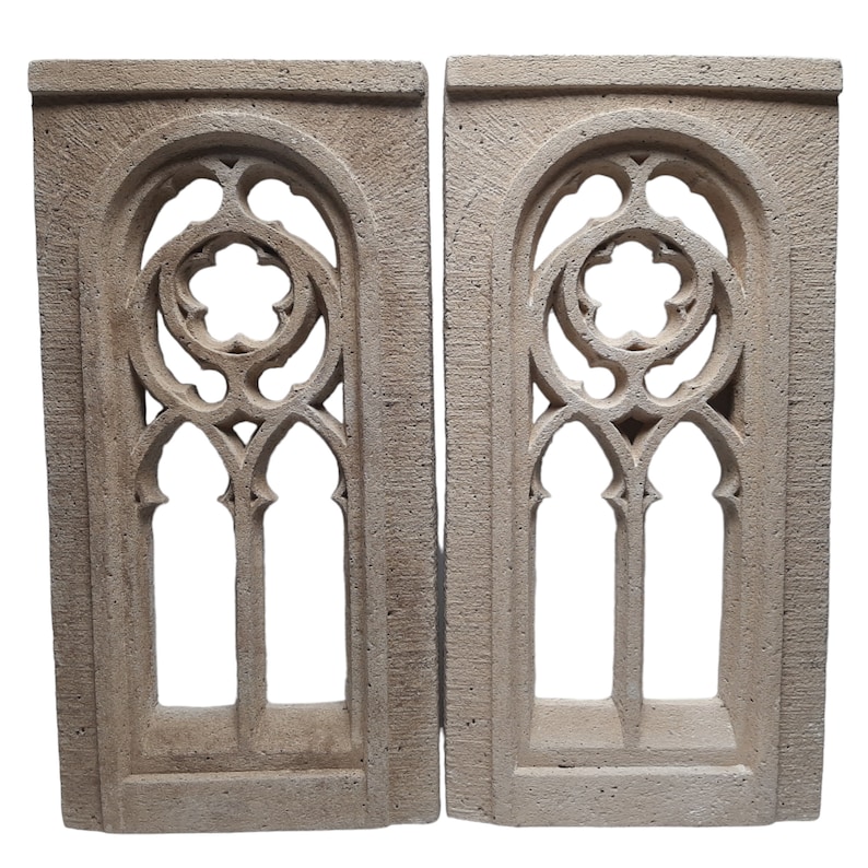 May include: Two beige stone arched window frames with intricate gothic style designs. The frames are made of a rough textured stone and have a slightly aged look.