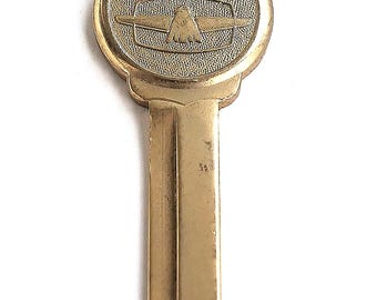 Può includere: Una chiave in metallo color ottone con una testa circolare dalla superficie testurizzata. La testa presenta un emblema di uccello stilizzato e la parola THUNDERBIRD in lettere rosse. La chiave ha una lama standard con una scanalatura centrale.